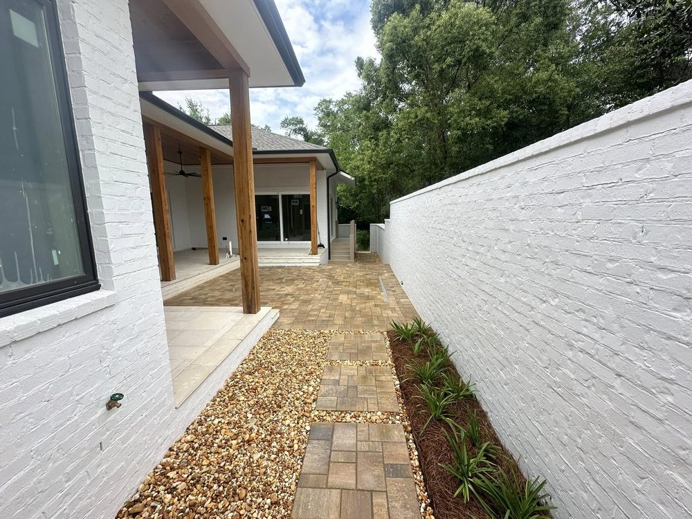Side-yard paver walkway with river rock and a white painted brick wall